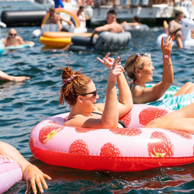 At a lively outdoor event, people are floating on inflatable tubes in the water, enjoying the ambiance. Perfect for those seeking DJ boat hire Sydney or a private yacht charter Sydney Harbour.