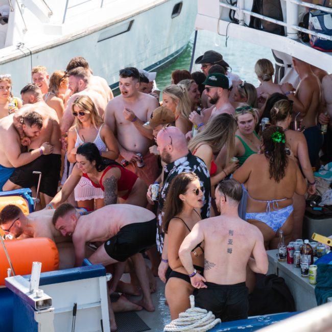 A lively boat party with people in swimwear gathered on the deck, some standing and some seated, with inflatable orange floats nearby. Enjoy a private yacht charter Sydney Harbour for an unforgettable experience.