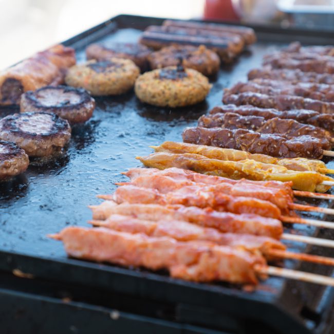 Delicious meats, including kebabs and burgers, sizzling on a large outdoor griddle during a Luxury yacht hire Sydney event.
