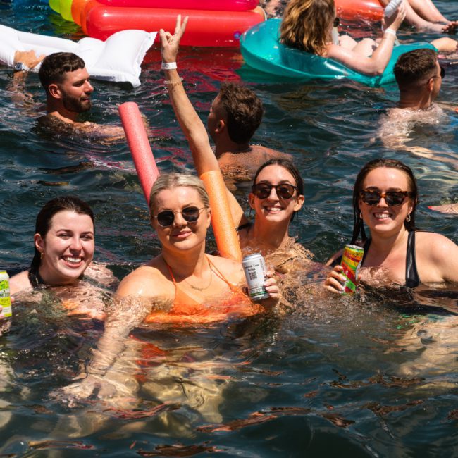 A group of people in swimsuits enjoy drinks while floating in a body of water with inflatable pool toys on a sunny day, part of a Private yacht charter Sydney Harbour.
