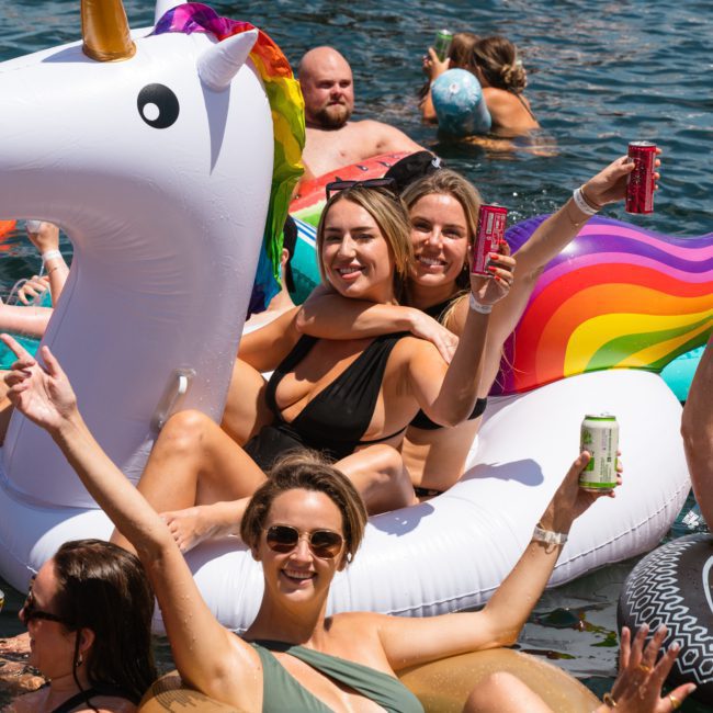 People enjoying a sunny day in a lake on inflatable floats, including a unicorn and rainbow float, holding drinks and smiling, reminiscent of the vibrant atmosphere you'd find at a Sydney boat party hire.