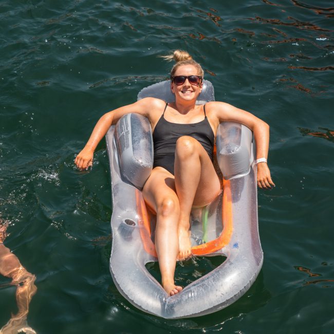 A person in a black swimsuit is relaxing on an inflatable pool float in the water, with sunglasses on and smiling, during a luxurious Sydney boat party hire.
