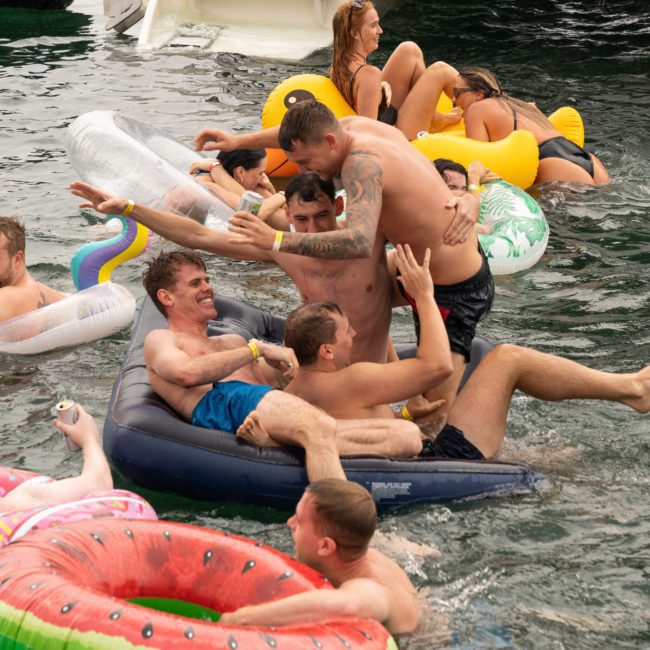 People enjoying a river party on inflatables near a private yacht charter Sydney Harbour. Several individuals are in the water, some on floating loungers, engaging in playful activities.