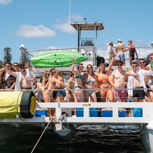 A group of people in swimwear standing on a luxury yacht hire Sydney, smiling and posing for a photo on a sunny day.