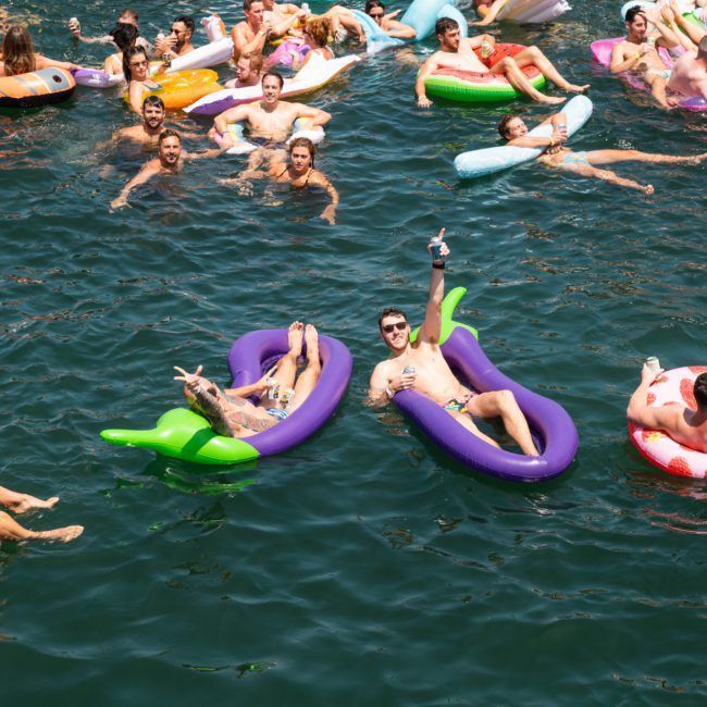 A large group of people float on inflatable pool toys in a body of water, enjoying a sunny day. Some hold drinks and relax while others interact with each other, reminiscent of the lively atmosphere you’d find at a Sydney boat party hire.