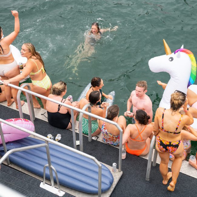 A group of people in swimsuits enjoying a Sydney boat party hire in a body of water.