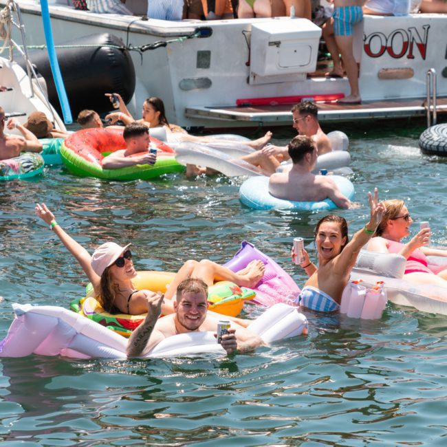 People are enjoying a sunny day on the water, lounging on inflatable floats and relaxing near boats, creating unforgettable moments at a DJ boat hire Sydney event.