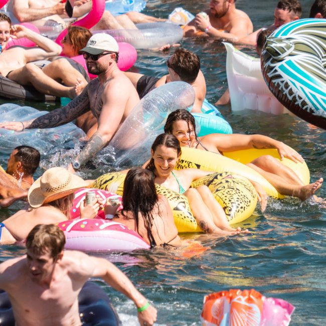 People are enjoying a sunny day floating on inflatables in the water, with some in swimsuits and others with hats. The scene is lively with various colorful inflatables, reminiscent of a Luxury yacht hire Sydney experience.