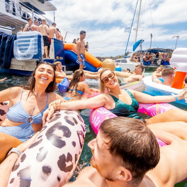 People enjoying a sunny day on the water with inflatable floats near boats, laughing and interacting with each other during a private yacht charter on Sydney Harbour.