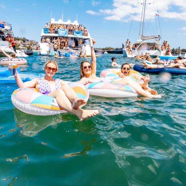 Three people relax on inflatable floats in the water, surrounded by other boats and individuals enjoying a sunny day, enhanced by corporate boat events Sydney.