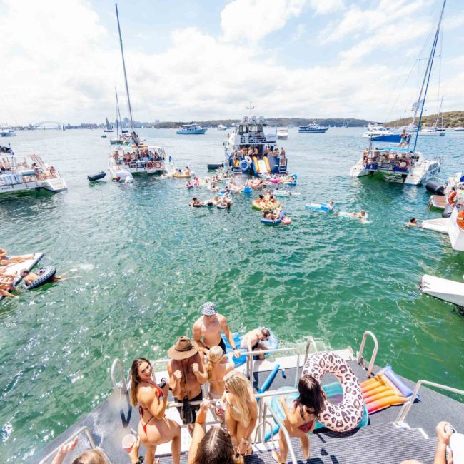 A group of people on a catamaran, surrounded by several other boats, enjoying a sunny day on the water. Perfect for those looking into Sydney boat party hire.