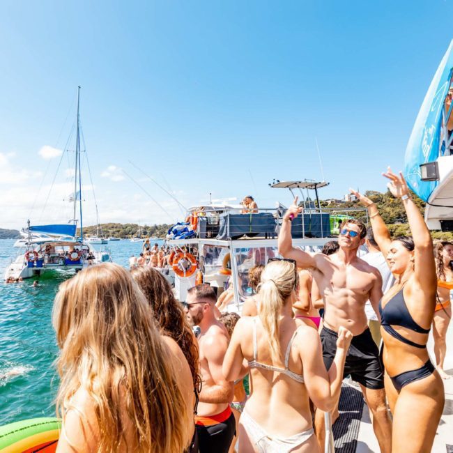 People are enjoying a sunny day on a crowded boat party, with several individuals swimming in the water nearby, thanks to Sydney boat party hire.
