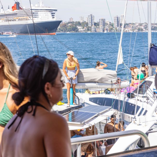 People enjoying a sunny day on a private yacht charter in Sydney Harbour with a cruise ship in the background and city buildings in the distance.
