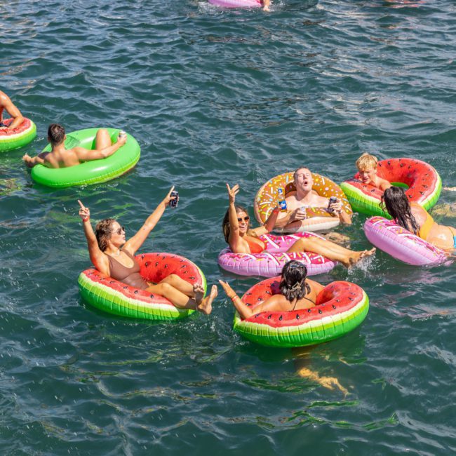 A group of people relaxes on colorful inflatable rings in the water, with some holding drinks, enjoying a Sydney boat party hire.