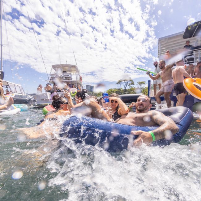 People enjoying a daytime Sydney boat party hire, with some on inflatables in the water, splashing and socializing.