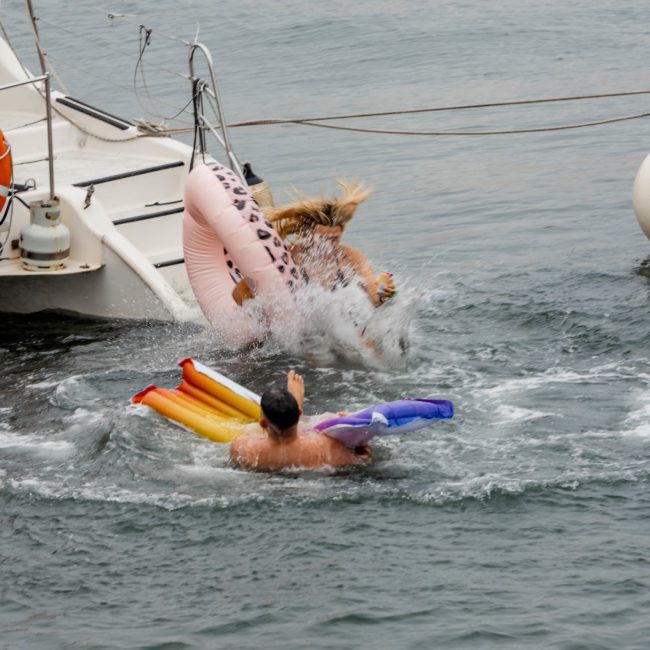Two people are in the water near a boat, one on an inflatable float and another falling from a luxury yacht hire in Sydney.