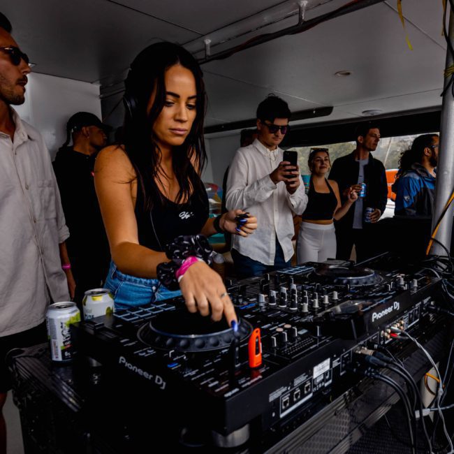 A DJ performs at a mixer console as people around her enjoy the music at an indoor event, reminiscent of the vibrant energy found on a luxury yacht hire Sydney.
