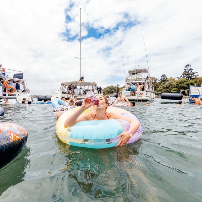 People enjoy a sunny day on the water, floating on inflatables and swimming near anchored boats during a private yacht charter in Sydney Harbour.