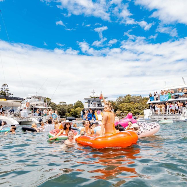 People reveling in a sunny day on a lake, lounging on inflatable rafts and swimming near several boats, reminiscent of the luxury yacht hire Sydney experience.