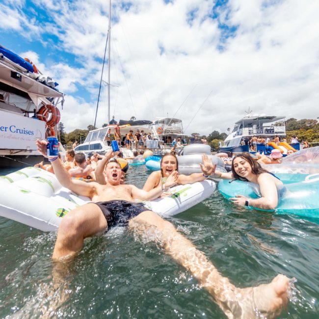 People are floating on inflatable tubes and enjoying their time in the sun near a luxury yacht hire in Sydney.