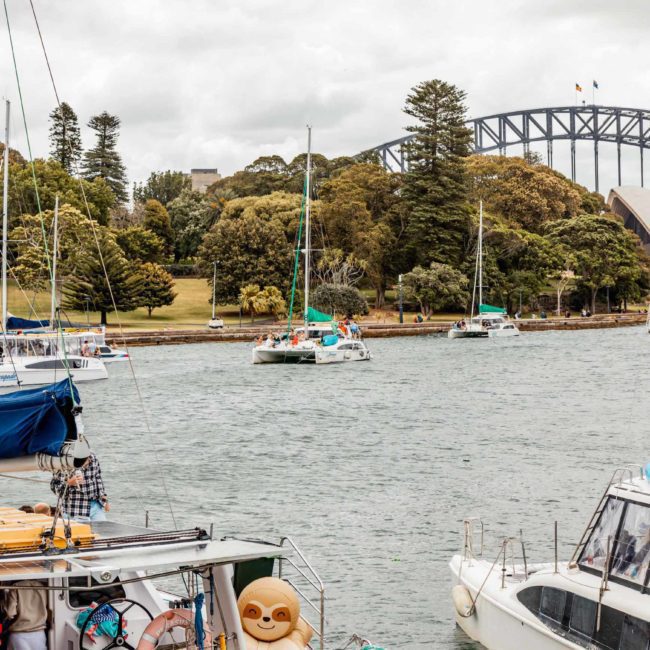 Several sailboats are moored in a harbor with the Sydney Opera House and Sydney Harbour Bridge visible in the background, offering a perfect setting for luxury yacht hire Sydney amidst cloudy weather.