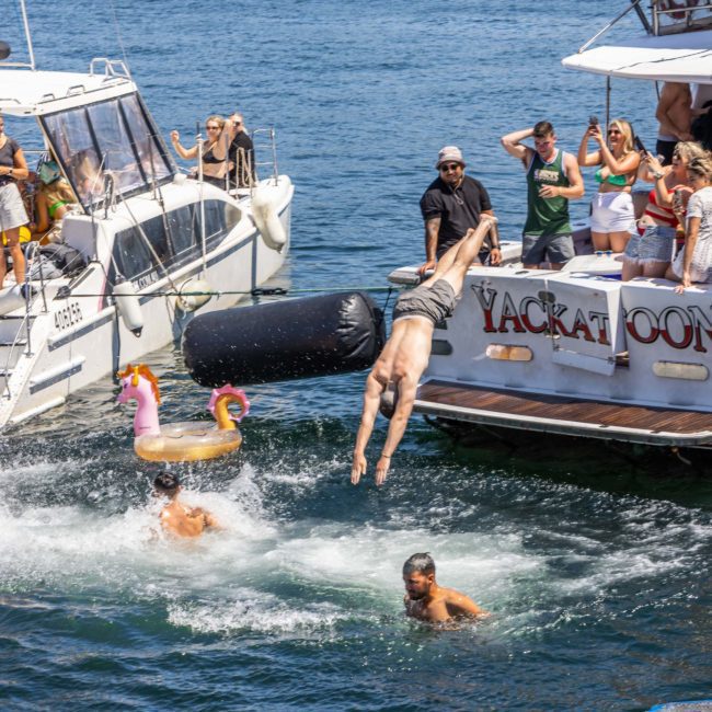 People on boats enjoying a sunny day on the water, with some jumping into the lake and others watching. Discover the fun with a Sydney boat party hire for an unforgettable experience.