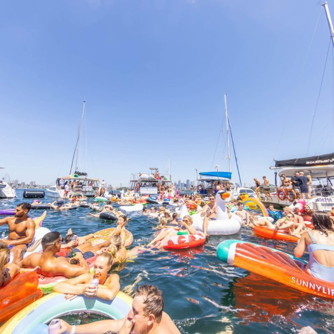 Enjoy a sunny day on the water with people lounging on inflatables, surrounded by anchored boats. Experience the excitement of DJ boat hire in Sydney, where vibrant music sets the perfect backdrop for fun and relaxation.