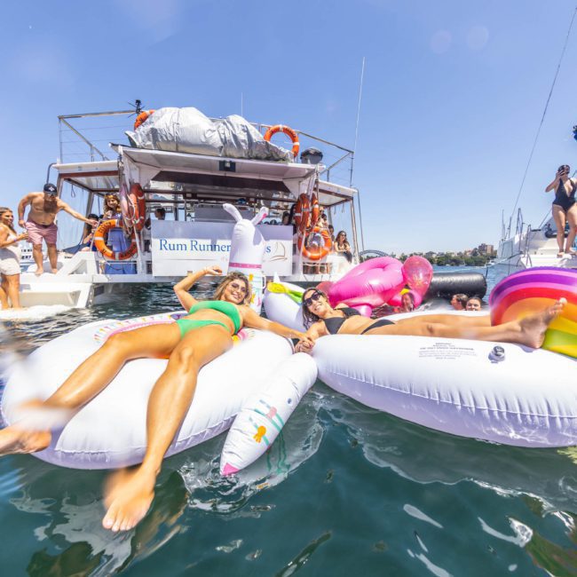People relaxing on inflatable floats in the water near a luxury yacht hire Sydney on a sunny day.