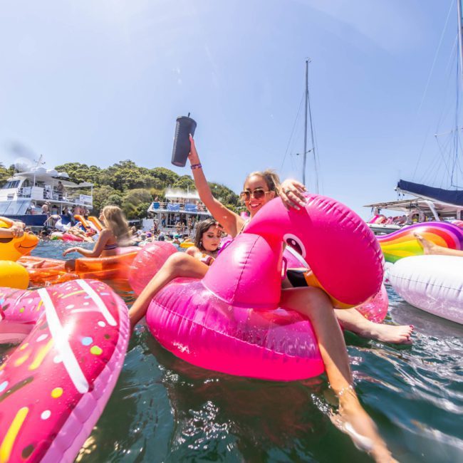People enjoying a sunny day on an inflatable float at a pool party, surrounded by colorful floats and boats in the background. It's the perfect scene for a Sydney boat party hire or DJ boat hire Sydney, making any corporate boat events in Sydney unforgettable.