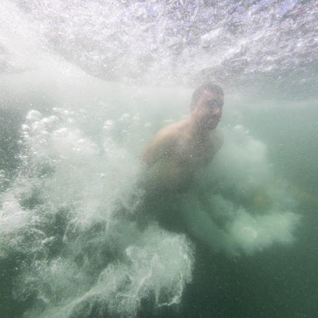 A person is captured underwater amidst bubbles and splashes, suggesting a recent dive or jump into the water during a lively Sydney boat party hire.