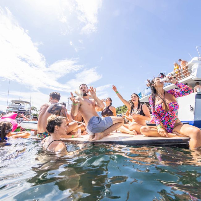 A group of people enjoys a sunny day on a luxury yacht in Sydney Harbour, surrounded by inflatables and other boats.
