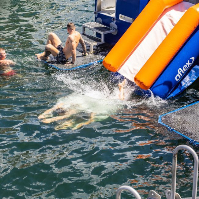 People enjoying an inflatable slide into the water from a private yacht charter Sydney Harbour.