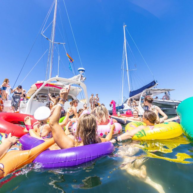 A group of people float on colorful inflatable pool toys in the water near several boats on a sunny day, enjoying what seems like an incredible Sydney boat party hire.
