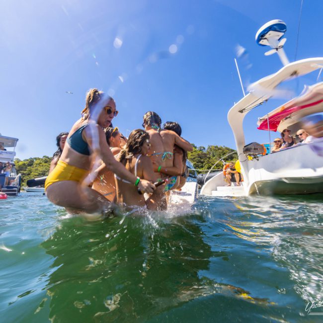 A group of people in swimsuits are having fun in waist-deep water near boats on a sunny day, enjoying a luxury yacht hire Sydney experience.