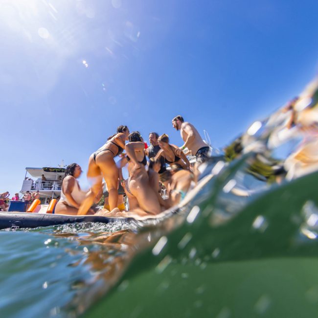 A group of people wearing swimwear gathered on a floating platform in the water, with a luxury yacht hire Sydney and clear blue sky in the background.