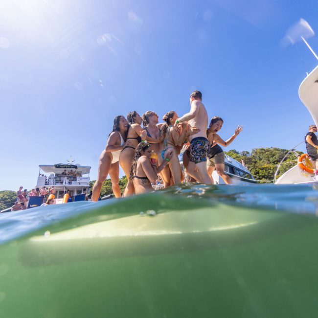 Group of people in swimwear standing on a boat, gathered together and appearing to have fun under a clear blue sky during a luxury yacht hire in Sydney.
