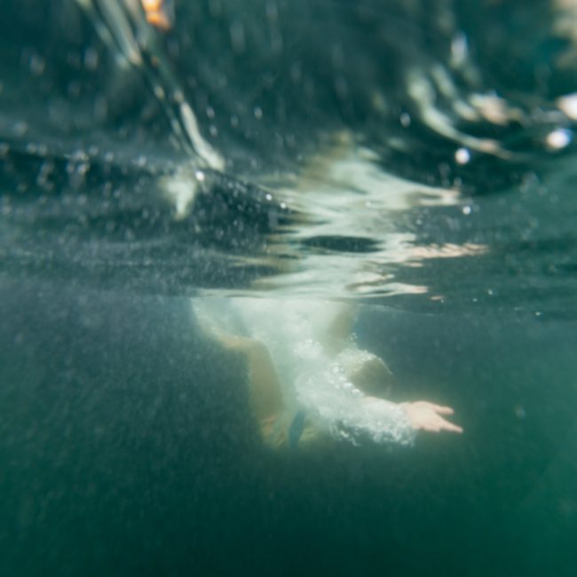 A person swimming underwater, partially submerged with their arm extended forward, creating bubbles in a body of water. Ideal for a refreshing break during corporate boat events Sydney.