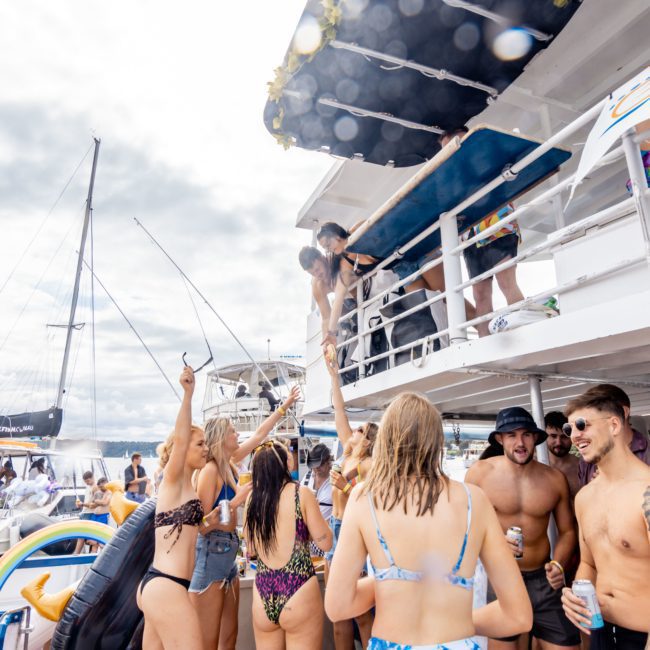 People on a boat having a party, with some dancing and others socializing. Another boat is visible in the background, showcasing the excitement of Catamaran party Sydney events.
