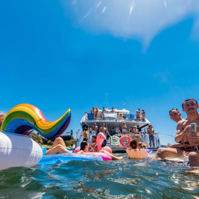 People enjoying a sunny day on a private yacht charter Sydney Harbour, with colorful inflatables and drinks.