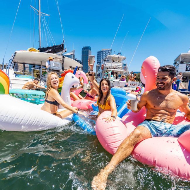 People enjoying a sunny day on colorful inflatable floats in a bay, with boats moored in the background, perfect for a Catamaran party Sydney.