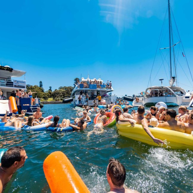A group of people enjoying a sunny day on inflatables in the water, surrounded by boats from a Sydney boat party hire.