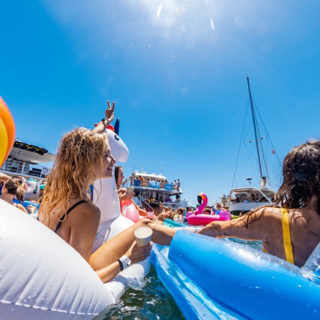 People enjoying a sunny day on the water with colorful inflatable floaties, surrounded by boats, during a lively Sydney boat party hire.