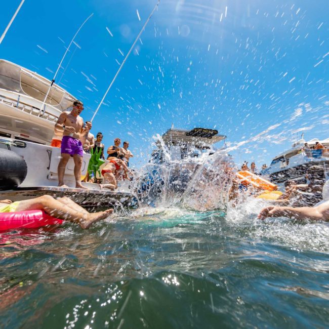 People on inflatable floats and boats enjoy a sunny day on the water, with splashes of water captured mid-air, adding to the festive atmosphere of a catamaran party in Sydney.