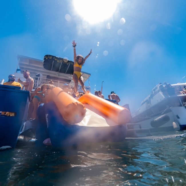 People enjoying a luxury yacht hire Sydney on a sunny day, with some individuals seen jumping from an inflatable slide into the water.