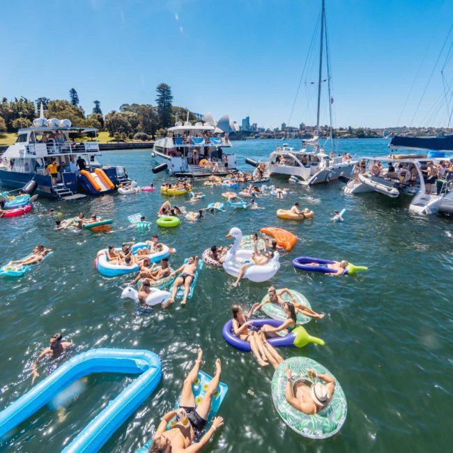 People on floaties and boats, including a luxury yacht hire Sydney, enjoying a sunny day on the water.