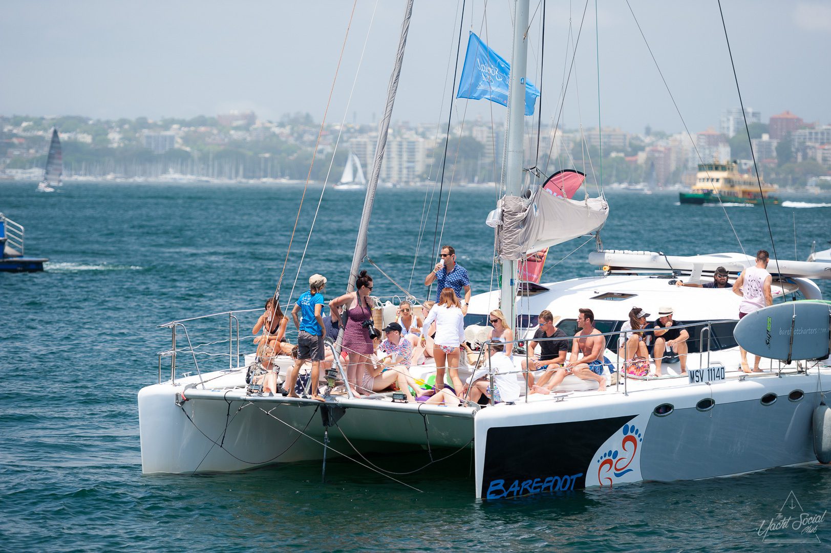 A group of people relaxes and socializes on a luxury yacht hire in Sydney Harbour, afloat on a calm sea near a coastal city.
