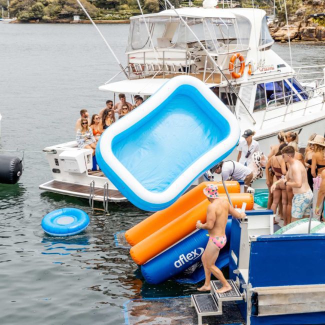 People on boats engaged in activities, with an inflatable pool and slide connected to a yacht in a body of water, perfect for Sydney boat party hire or corporate boat events in Sydney.