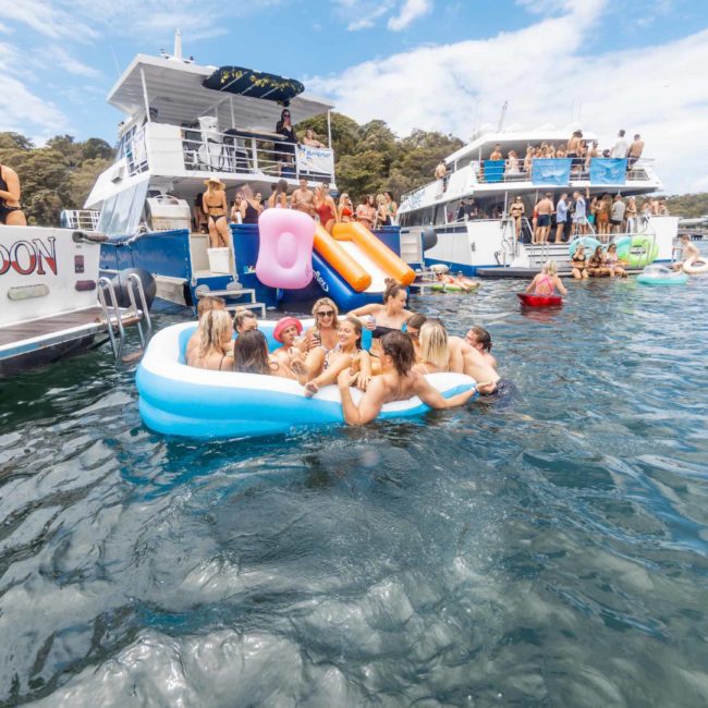 Groups of people enjoying a Sydney boat party hire on boats and inflatables on a sunny day in the water.