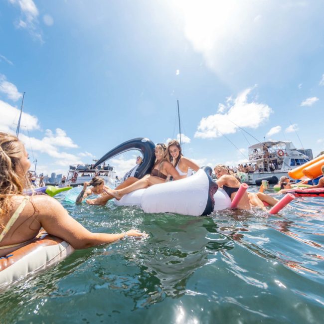 People enjoying a sunny day on the water with inflatable toys and boats in the background, making the most of their private yacht charter in Sydney Harbour.