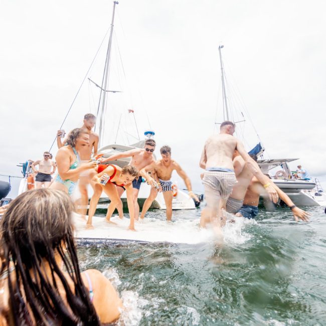 A group of people, including children, enjoying time on a luxury yacht in Sydney and in the water. Some are swimming while others are on the boat.